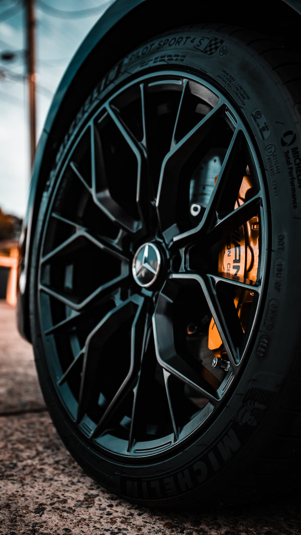 Close-up of a car wheel with a distinctive rim design on a road.