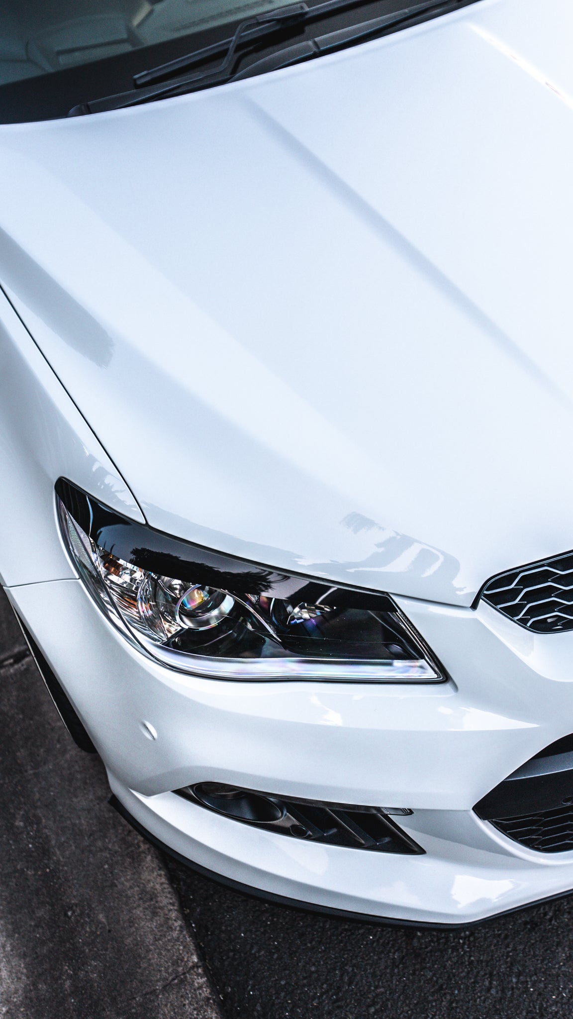 Close-up of a white car's headlight and front grille