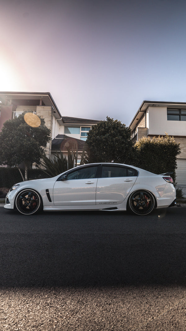 White car parked on a residential street with houses and trees in the background.